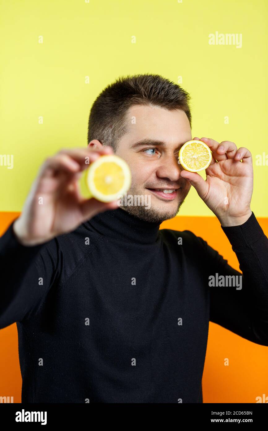 Portrait d'un homme élégant sur fond jaune en raglan noir avec une tranche de citron dans les mains. Style. Un sourire sur son visage. Une image pour un m Banque D'Images