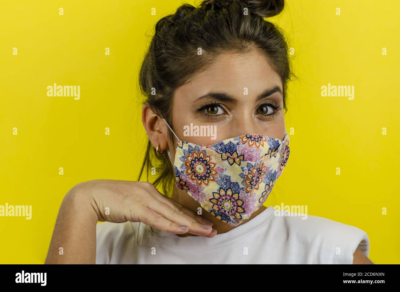 Femme hispanique avec masque facial et expression sérieuse sur jaune arrière-plan Banque D'Images