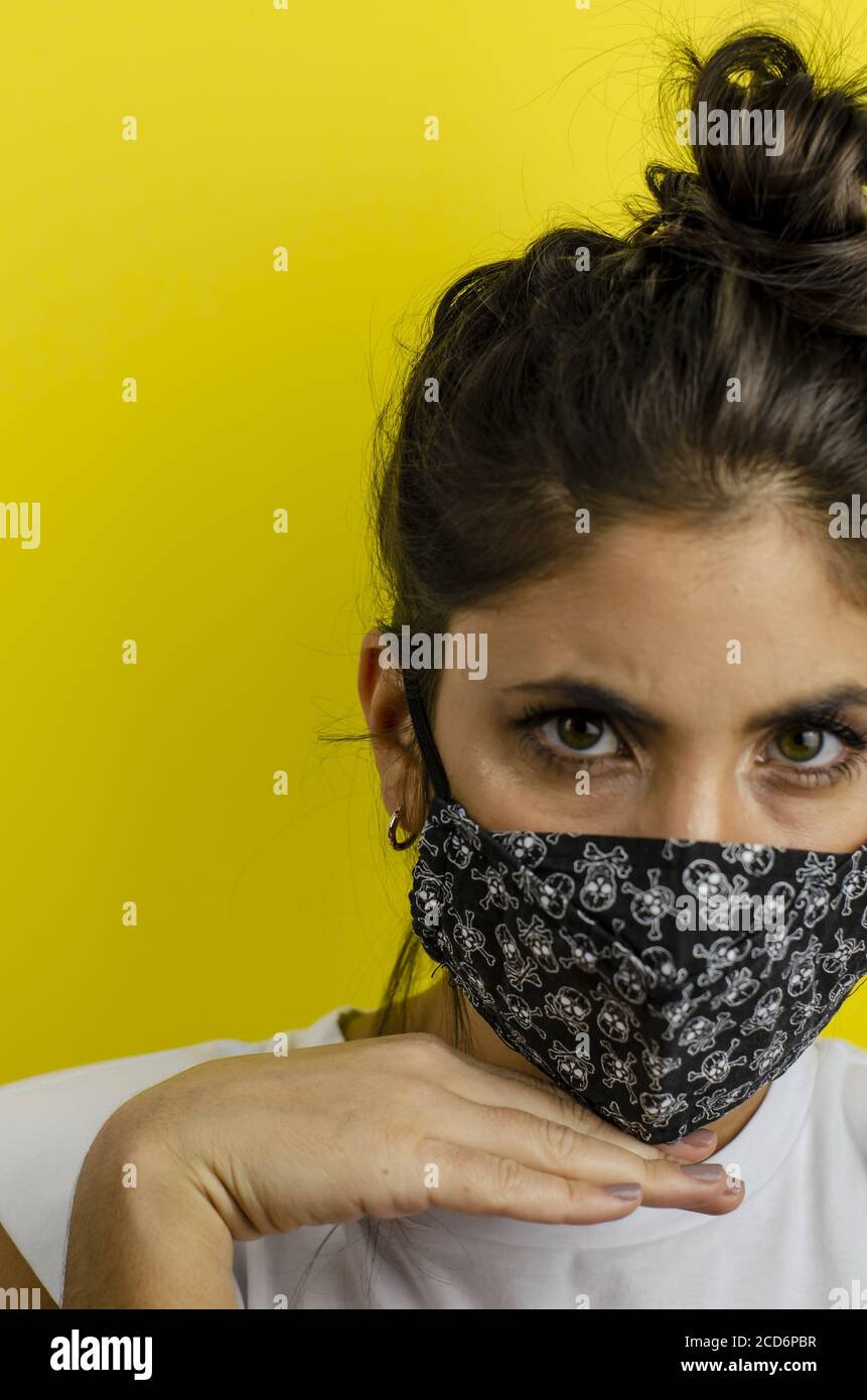 Prise de vue verticale d'une femme hispanique avec masque facial et expression sérieuse sur fond jaune Banque D'Images