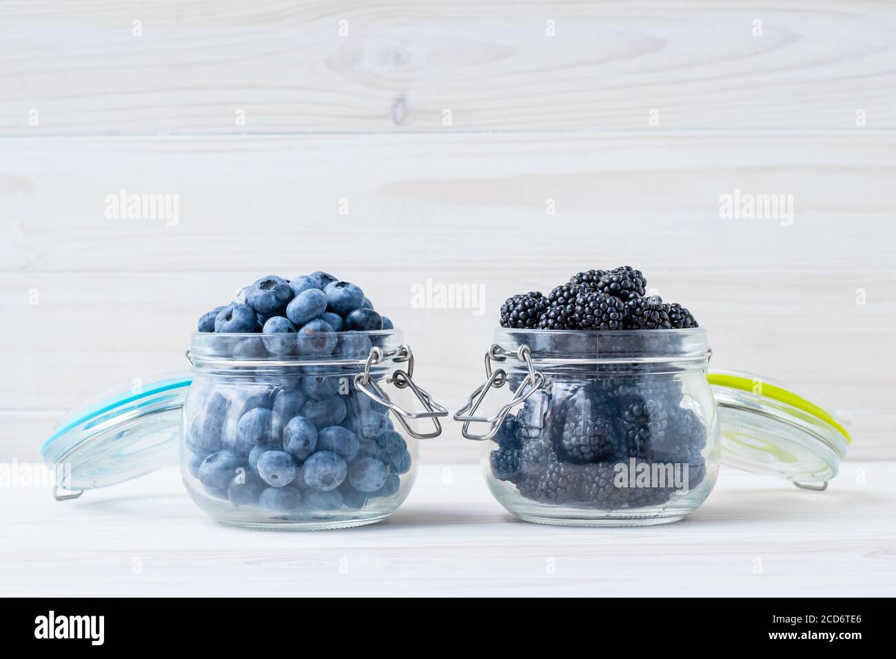 Bleuets et mûres dans un bol sur une table en bois blanc. Baies dans une verseuse en verre. Concept de cuisine végétarienne. Espace de copie, espace vide pour le texte Banque D'Images