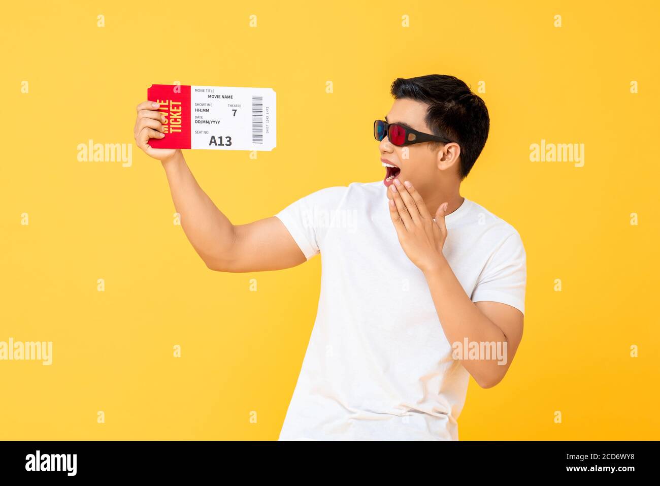 Portrait amusant de jeune asiatique surpris portant des lunettes 3D tenue d'un billet de cinéma sur fond jaune studio isolé Banque D'Images