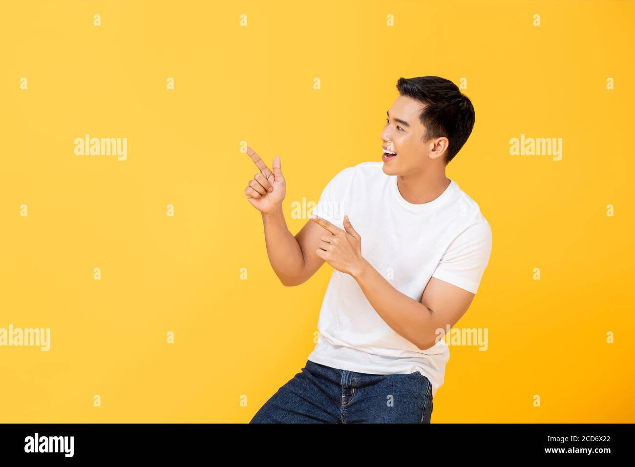 Portrait de côté d'un jeune homme asiatique souriant et charmant pointant vers l'avant les doigts dans l'espace vide mis à part dans un arrière-plan isolé de studio jaune Banque D'Images