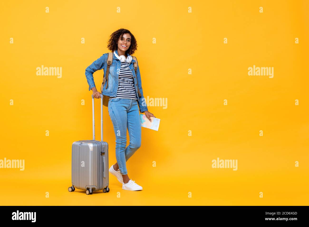 Portrait complet de voyage de jeune femme afro-américaine souriante backpacker debout et tenant des bagages sur fond jaune studio Banque D'Images