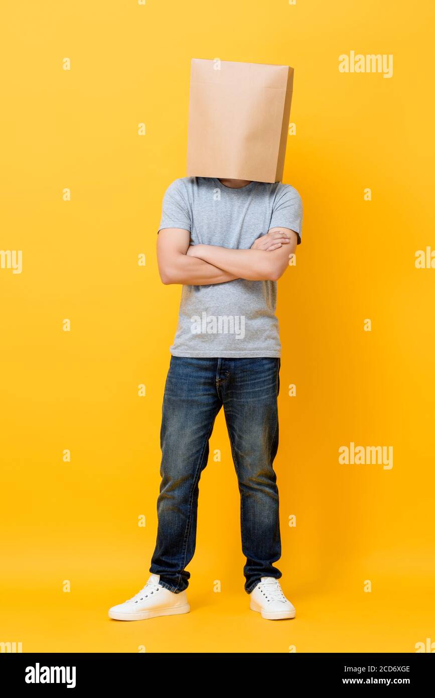 Concept portrait complet de l'homme anonyme avec la tête couverte avec sac en papier faisant des bras croisés geste dans jaune studio arrière-plan Banque D'Images