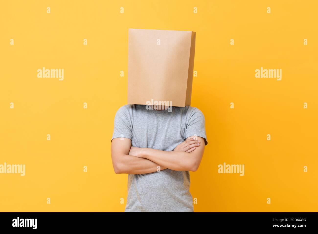 Portrait de concept de l'homme anonyme avec la tête couverte de papier sac faisant des bras mouvement croisé sur fond jaune studio Banque D'Images