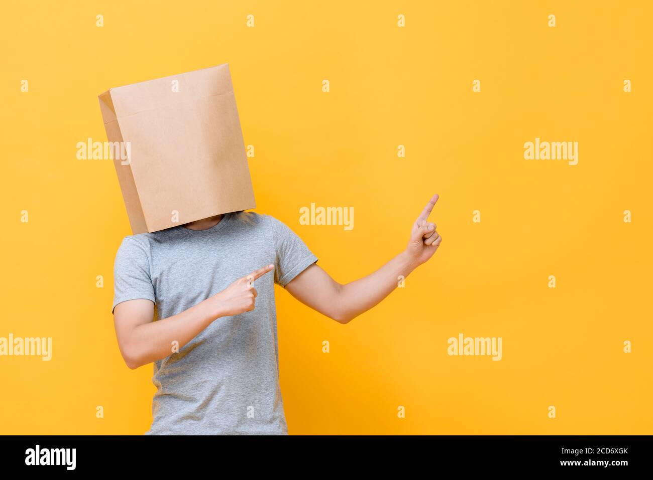 Portrait de concept de l'homme anonyme avec la tête couverte de papier sac pointant les deux doigts vers le haut sur fond jaune studio Banque D'Images