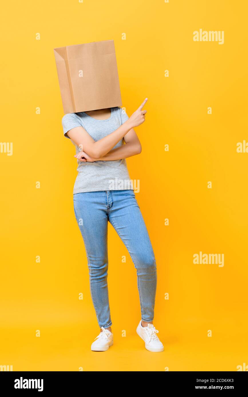 Portrait de concept de la femme anonyme avec la tête couverte de papier sac pointant vers le haut sur fond jaune du studio Banque D'Images