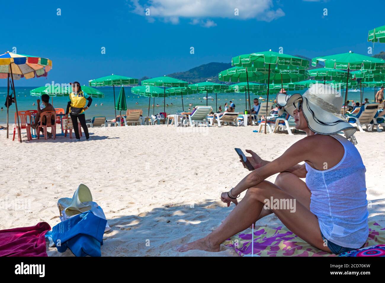 Touriste utilisant le téléphone portable à l'ombre sur la plage, Patong, Phuket, Thaïlande Banque D'Images