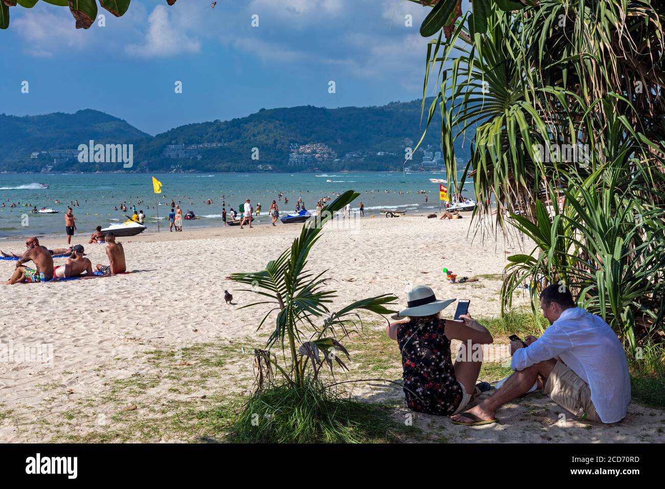 Couple touristique sur les téléphones portables à l'ombre à Patong Beach, Phuket, Thaïlande Banque D'Images