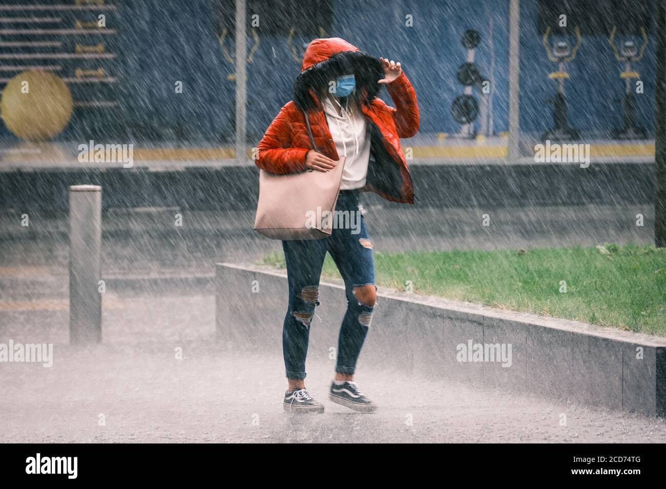 Météo au Royaume-Uni: Les jeunes femmes sous un manteau rouge et portant un masque facial sont prises dans une douche à forte pluie, Preston, Royaume-Uni Banque D'Images