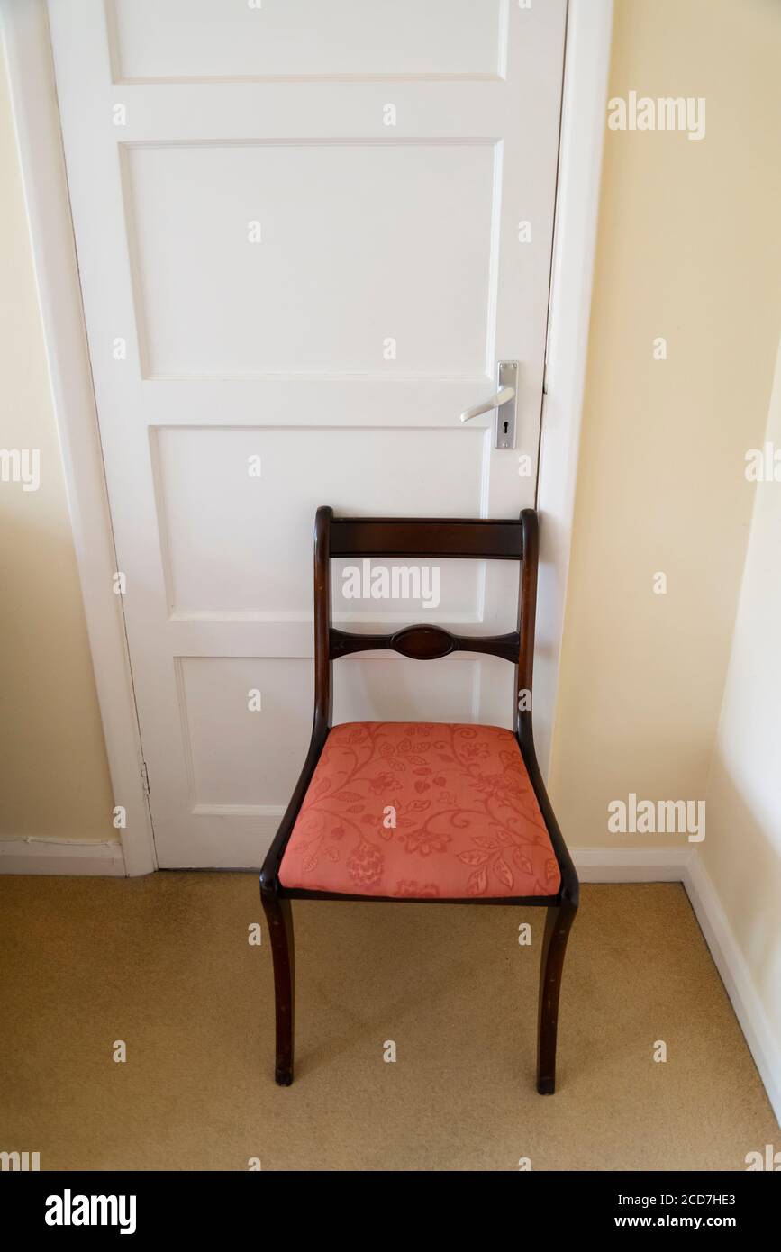 Chaise de salle à manger tenant une porte fermée dans une chambre dans une maison de banlieue, Londres, Angleterre, Royaume-Uni Banque D'Images
