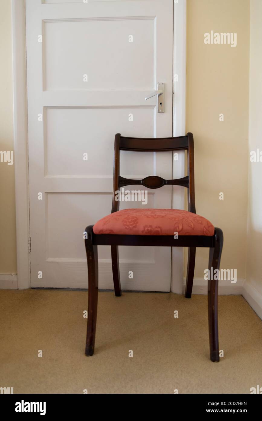 Chaise de salle à manger tenant une porte fermée dans une chambre dans une maison de banlieue, Londres, Angleterre, Royaume-Uni Banque D'Images