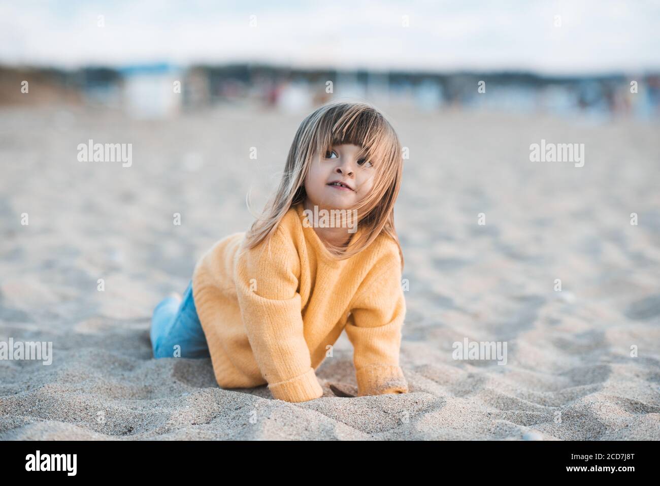 Mignon enfant fille de 2-3 ans vêtu d'un pull jaune tricoté et d'un  pantalon en denim amusant à la plage jouer avec le sable dehors de près.  Enfance. Automne se Photo Stock -