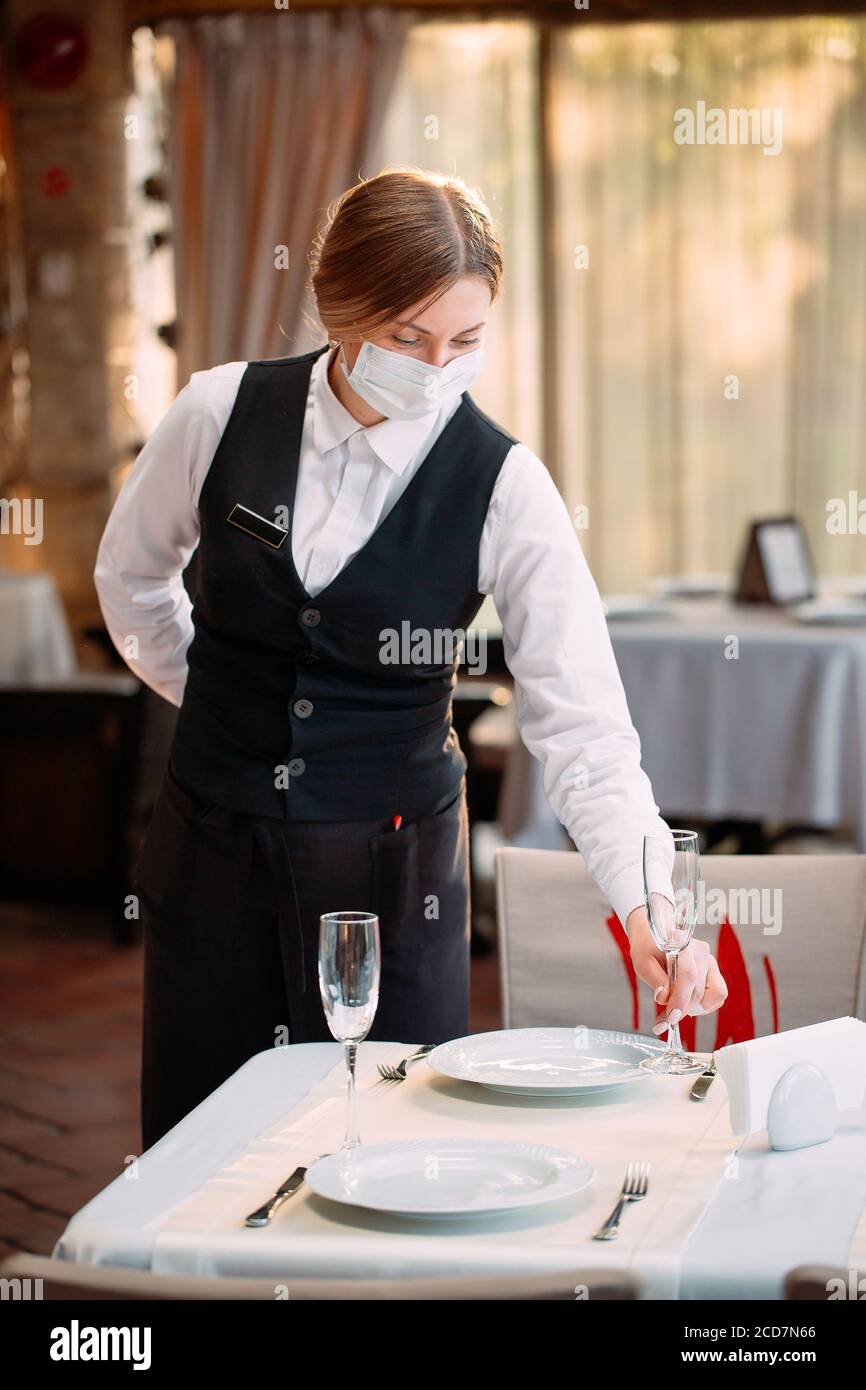 Un serveur dans un masque de protection médicale sert la table dans le restaurant. Banque D'Images