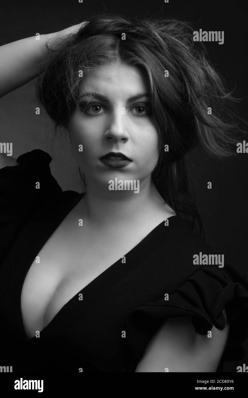 Portrait noir et blanc d'une femme en surpoids dans un studio sur fond noir. Elle recueille ses cheveux avec sa main Banque D'Images