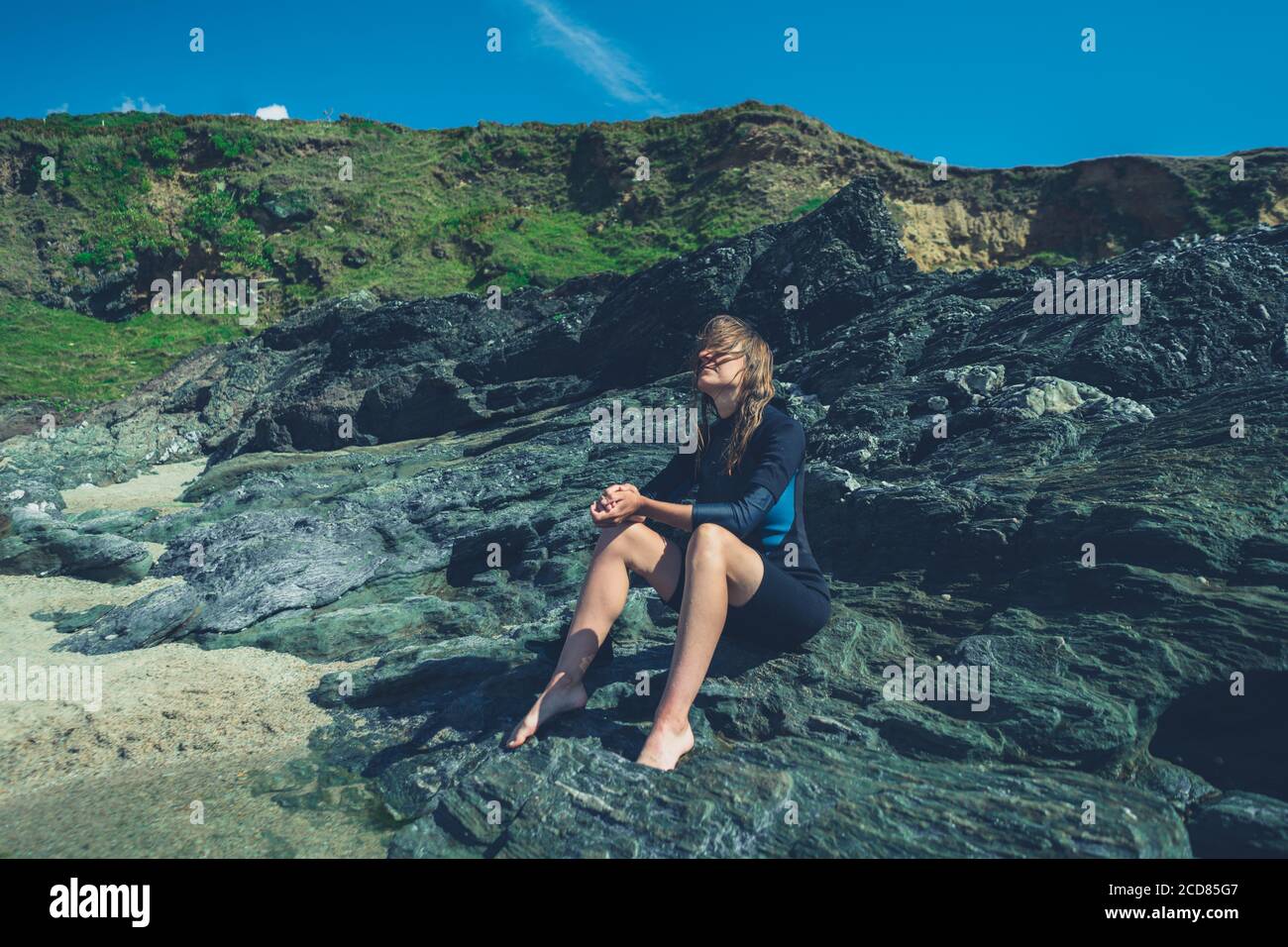 Une jeune femme est assise sur les rochers par mer en été avec une combinaison Banque D'Images