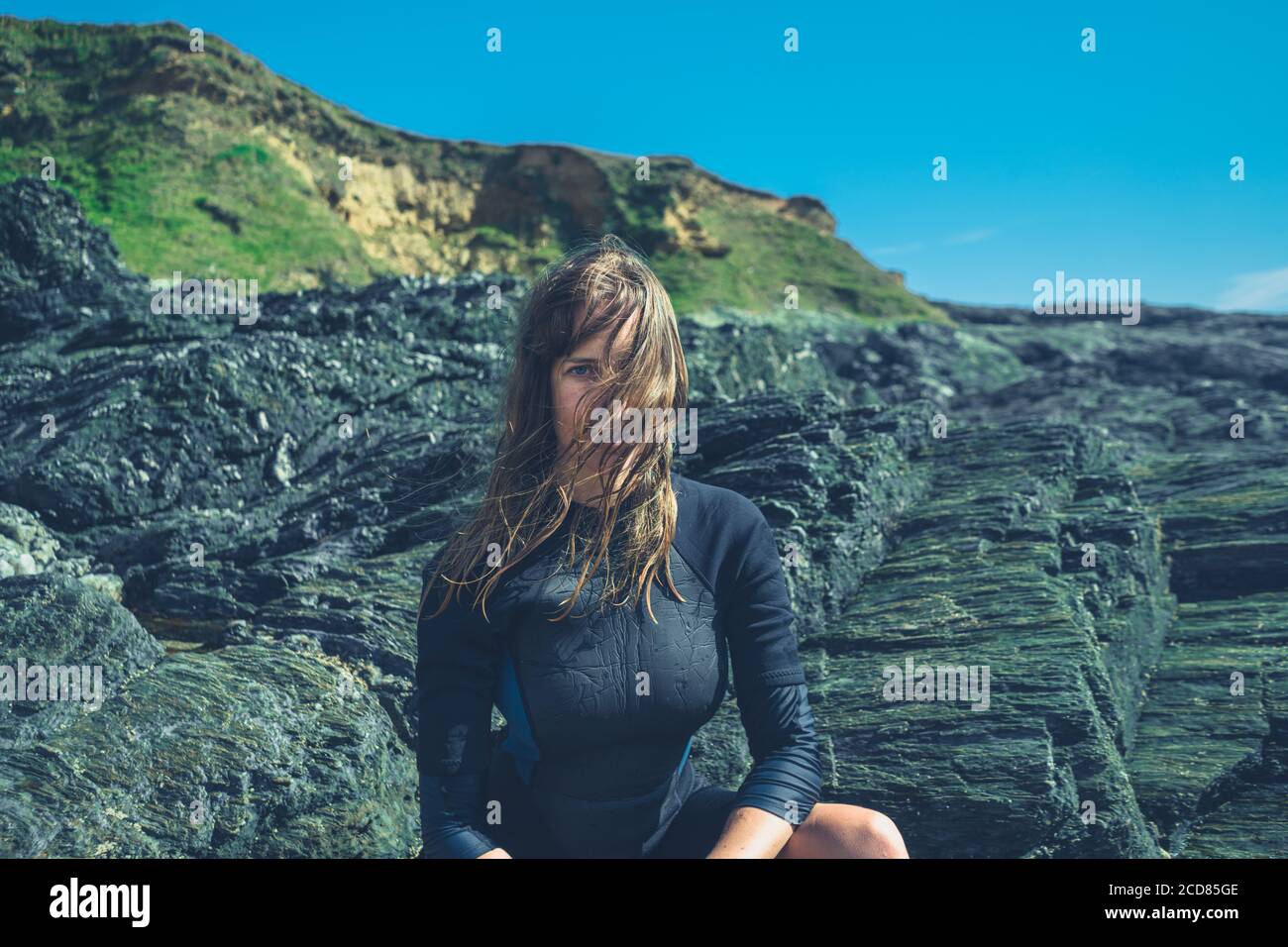 Une jeune femme est assise sur les rochers par mer en été avec une combinaison Banque D'Images