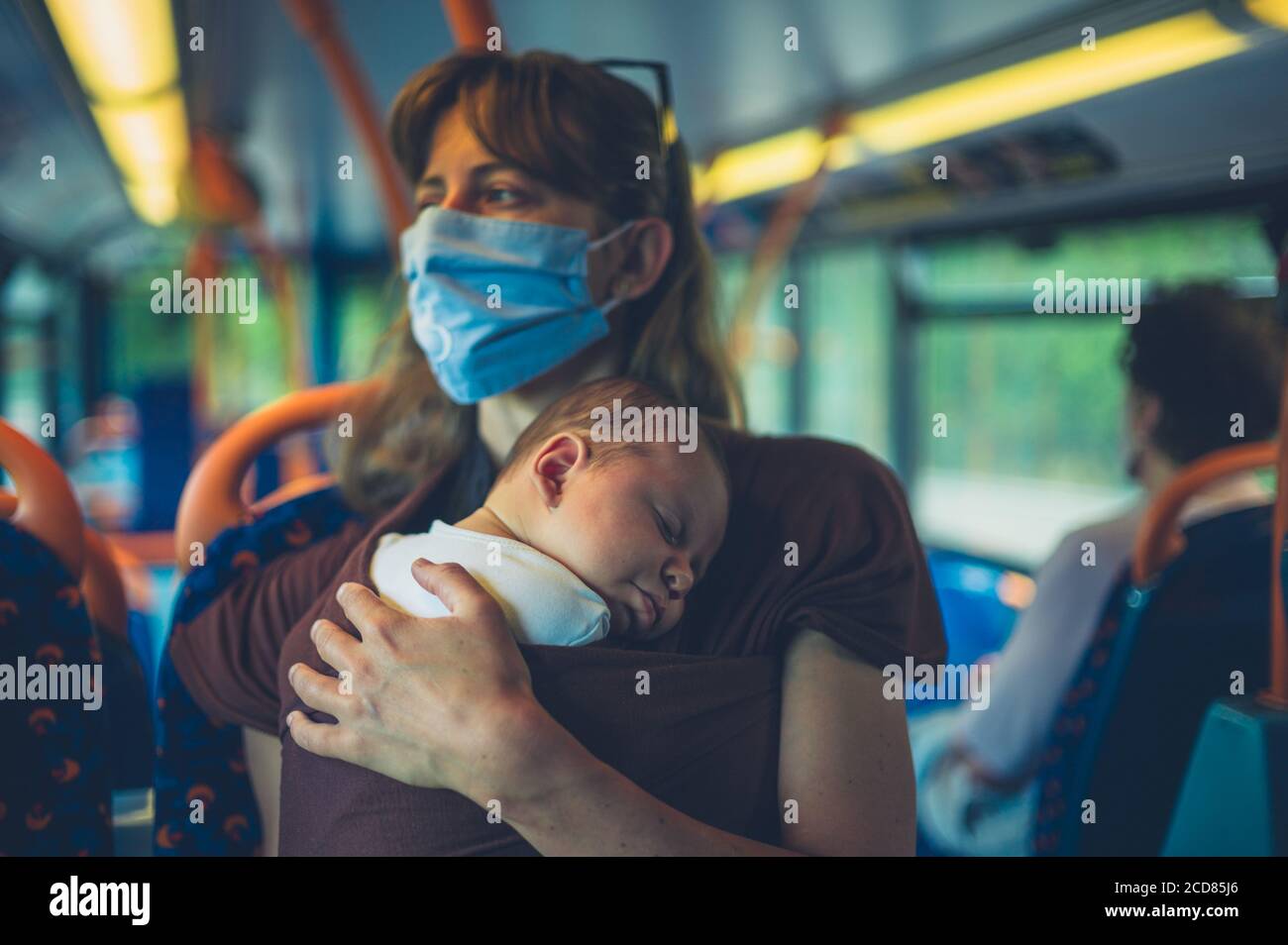 Une jeune mère avec son bébé dans une élingue est port d'un masque facial sur le bus Banque D'Images