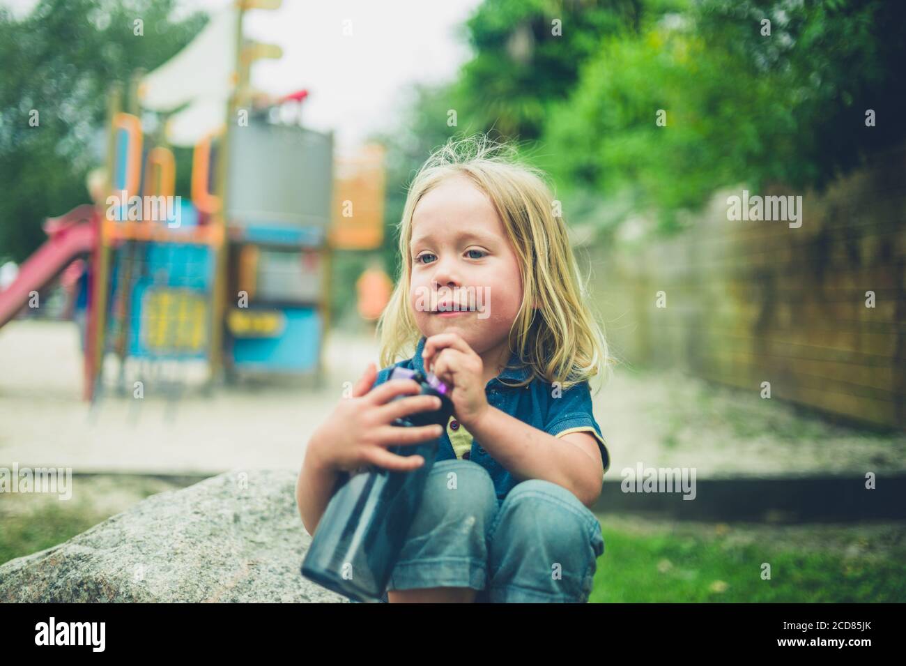 Un petit avant-chooler est assis à l'aire de jeux avec un bouteille d'eau Banque D'Images