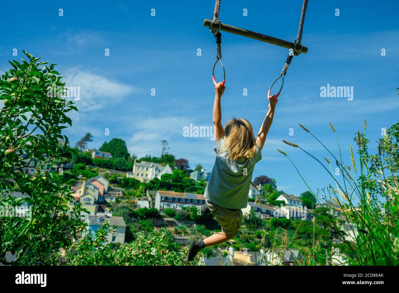 Un pré-chooler se balance d'un trapèze dans le jardin Banque D'Images
