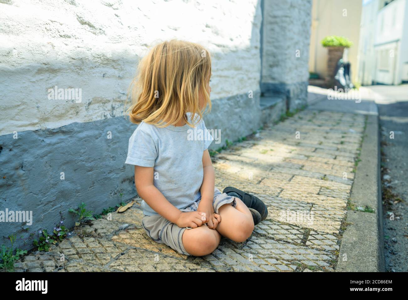 Un petit préchooler est assis sur la chaussée dans un ville Banque D'Images