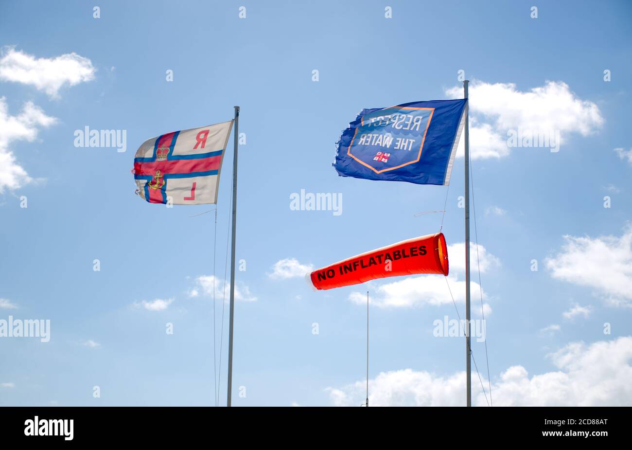 Les drapeaux RNLI, « No Inflatables » et « respect de l'eau » flottent dans le vent avec un ciel bue et un nuage clair en arrière-plan. Banque D'Images