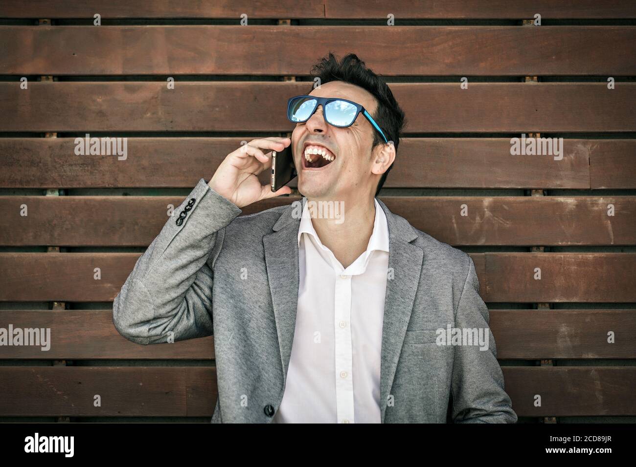 Joyeux homme adulte en costume élégant et lunettes de soleil riant avec  conattention tout en écoutant les bonnes nouvelles pendant la conversation  téléphonique Photo Stock - Alamy