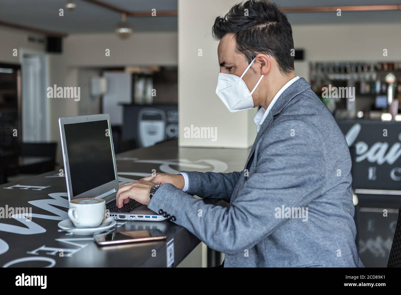 Vue latérale de l'entrepreneur masculin adulte ciblé en tenue habillée et masque de protection pour la saisie de la prévention des coronavirus sur le clavier de l'ordinateur portable tout en travaillant sur Banque D'Images