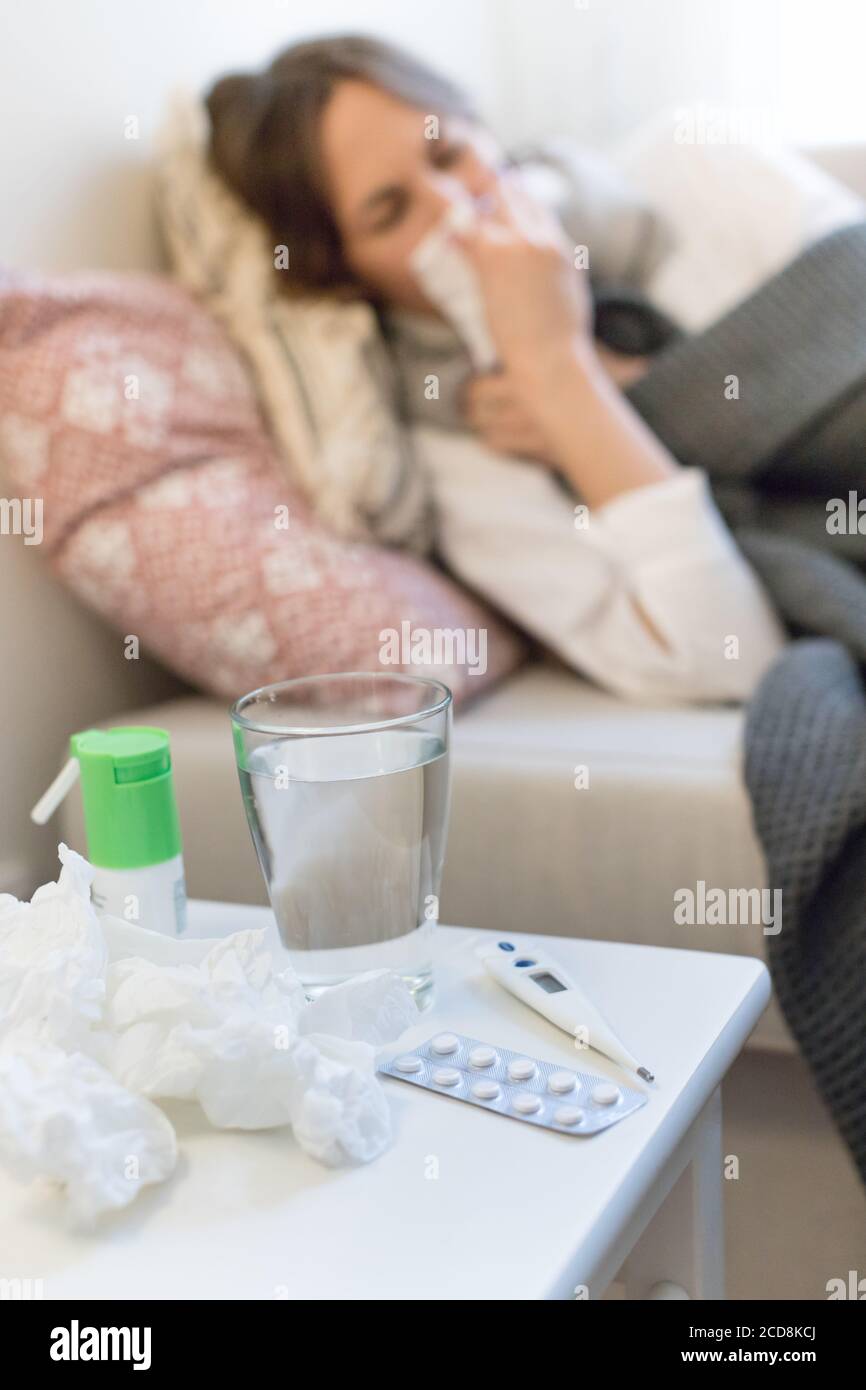 Femme malade floue allongé sur un canapé sous le plaid éternuant, se concentrer sur le thermomètre et les pilules. Saison de la grippe Banque D'Images