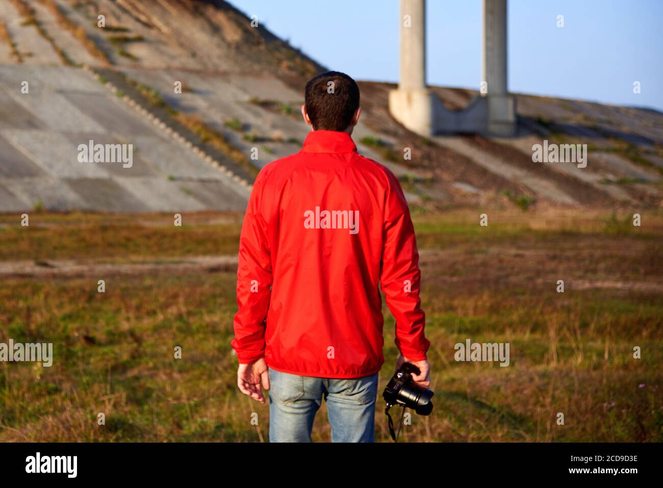 Un homme dans une veste rouge avec une caméra se tient près du pont au début de l'automne matin, vue arrière. Banque D'Images