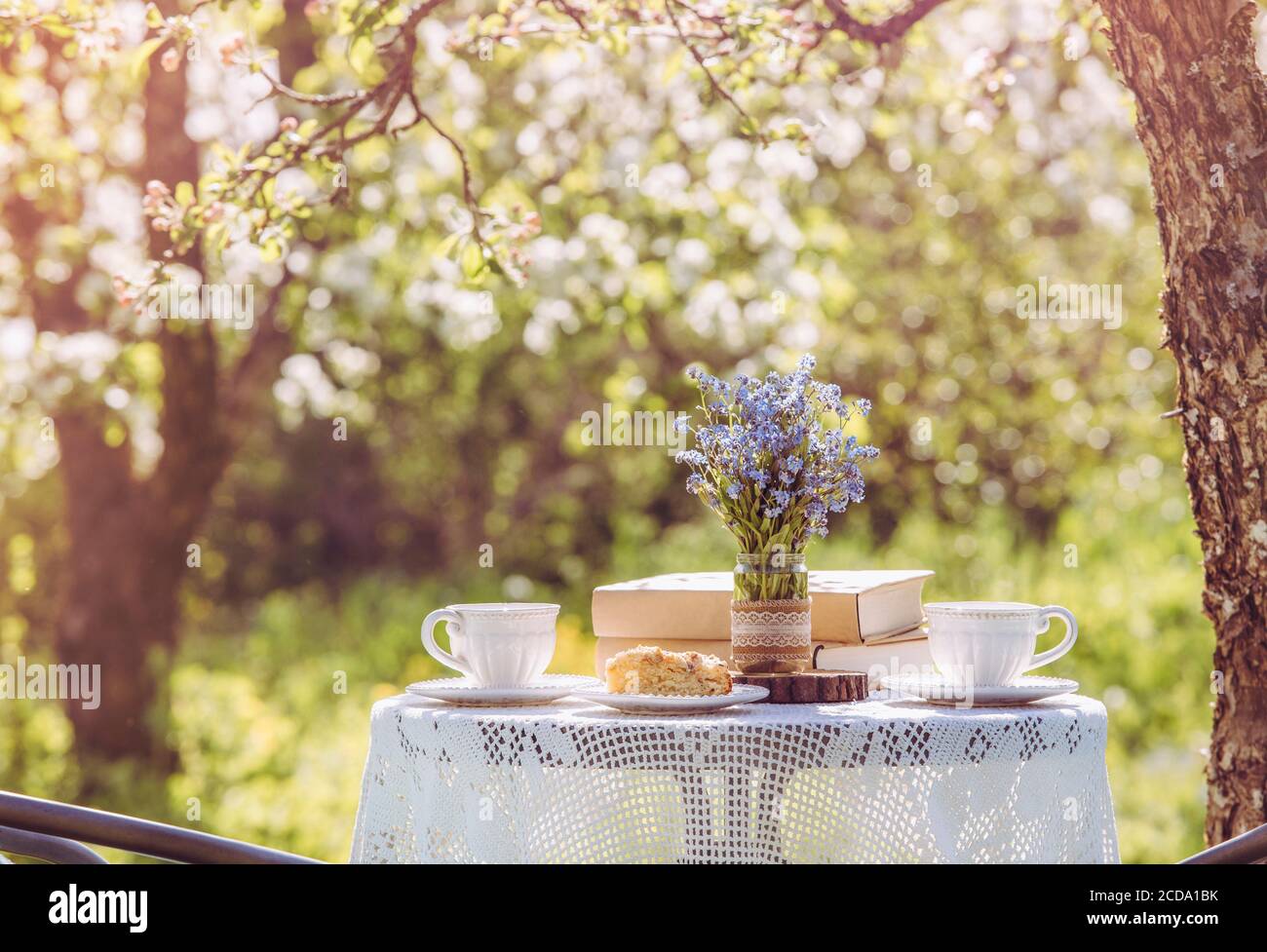 Printemps dans le jardin. Table avec tasses à thé, boho réutiliser vase pot avec Forget Me Not flowers ( Myosotis) et petite pile de livres. L'été, détendez-vous. Banque D'Images