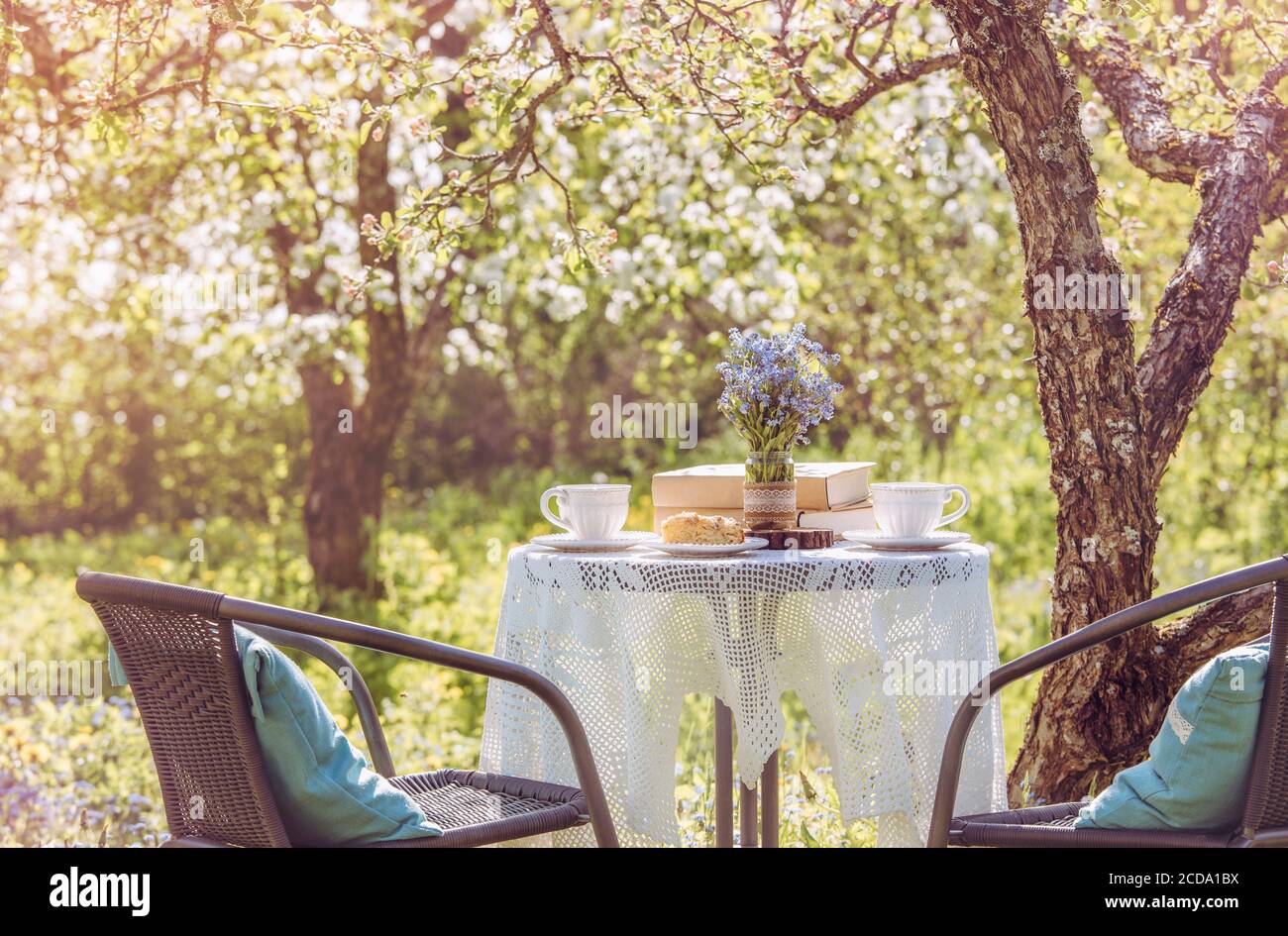 Printemps dans le jardin. Table avec tasses à thé, boho réutiliser vase pot avec Forget Me Not flowers ( Myosotis) et petite pile de livres. L'été, détendez-vous. Banque D'Images