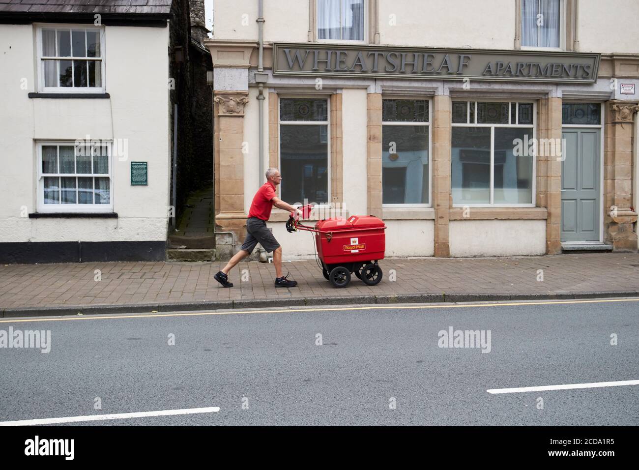 Postman poussant le chariot en montant le long de highgate Kendal cumbria angleterre royaume-uni Banque D'Images