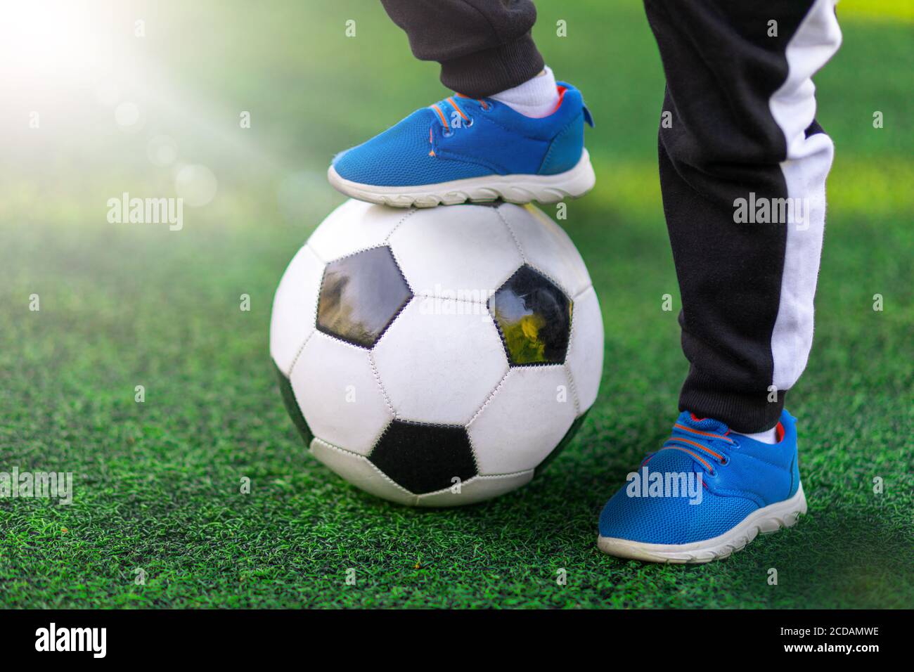 Le pied des enfants du vainqueur de la sneaker de chaussures de sport se tient sur un ballon de football contre un fond d'herbe. Gros plan sur le jeu et l'entraînement Banque D'Images