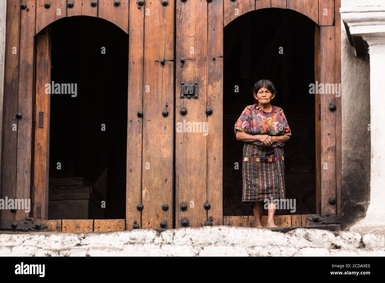 Une femme maya quiche âgée en robe traditionnelle se tient dans l'ancienne porte en bois de l'église de Santo Tomas à Chichichastenango, Guatemala. Banque D'Images