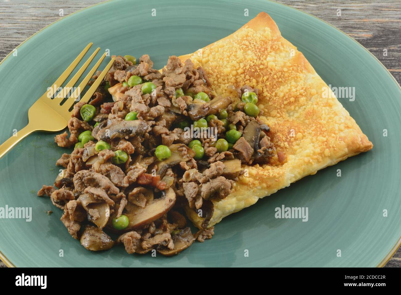 Ragoût de bœuf avec champignons et petits pois et oignons sur une bouffée feuille de pâte sur plaque bleue avec fourchette dorée Banque D'Images