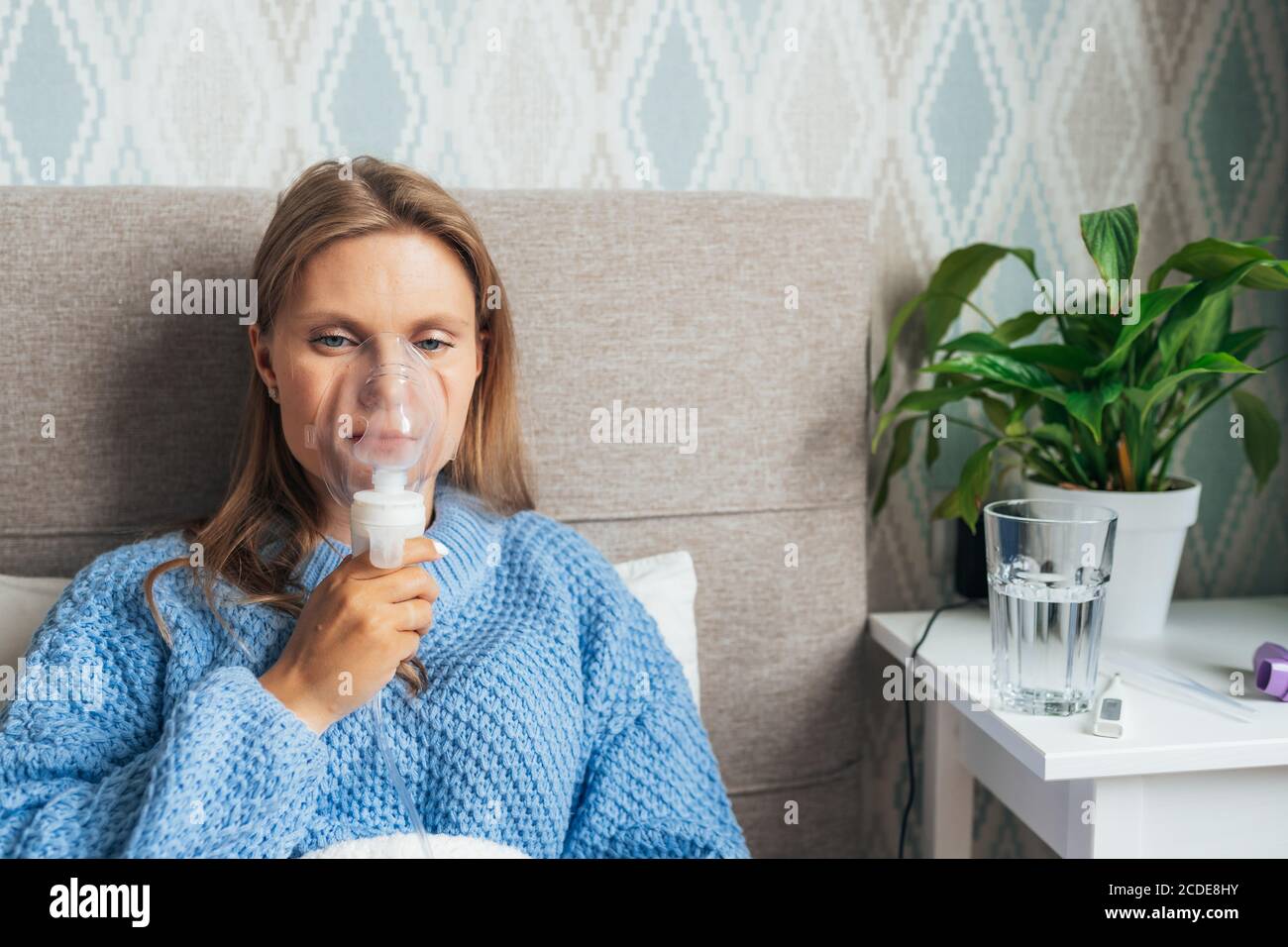 Jeune femme blonde en inhalation avec un nébuliseur à vapeur à la maison. Asthme, grippe, concept de soins de santé. Banque D'Images