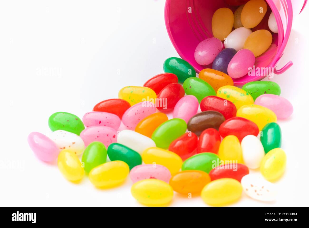 Bonbons colorés dans seau rose sur fond blanc et près du godet Banque D'Images