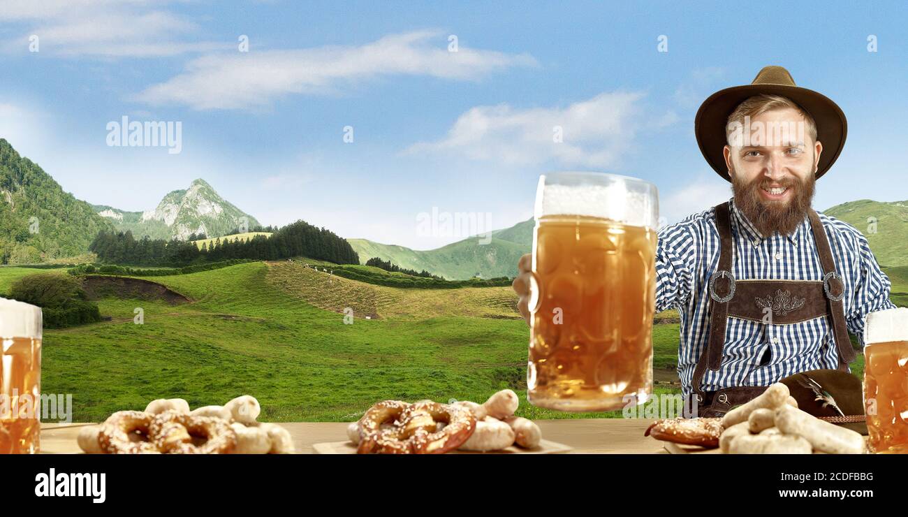L'homme souriant heureux avec une bière habillée dans un costume traditionnel autrichien ou bavarois tenant une tasse de bière, des montagnes sur le fond, flyer prêt pour la publicité. La fête, l'oktoberfest, le concept du festival. Banque D'Images