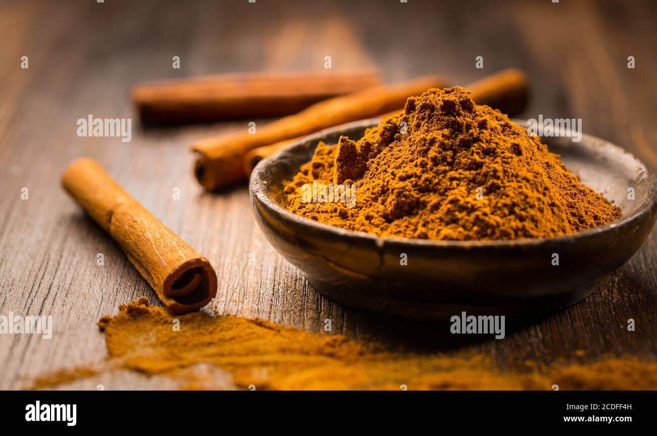 Poudre de cannelle dans un bol en bois avec des bâtons de cannelle sur fond de bois comme ingrédient de cuisson et de cuisson. Banque D'Images