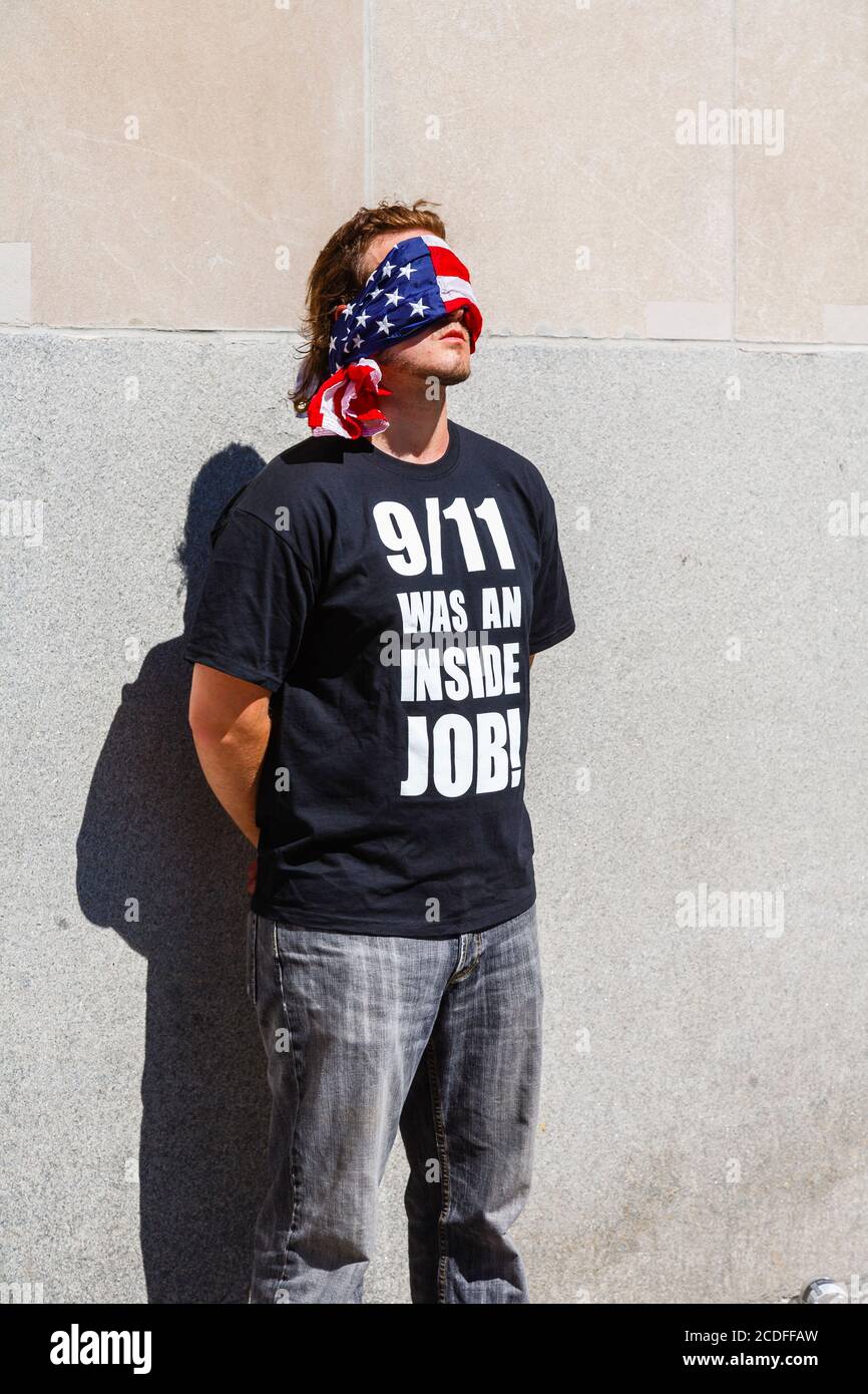 Un jeune homme américain se dresse sur le site du World Trade Center à New York, avec ses yeux bandés, portant un t-shirt noir sous la coupe : « 9/11 était un travail à l'intérieur ! » Banque D'Images