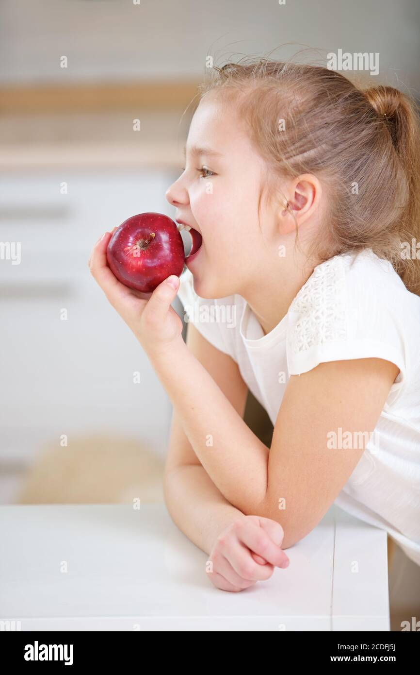 Une fille blonde se mord dans une pomme rouge fraîche dans le cuisine Banque D'Images