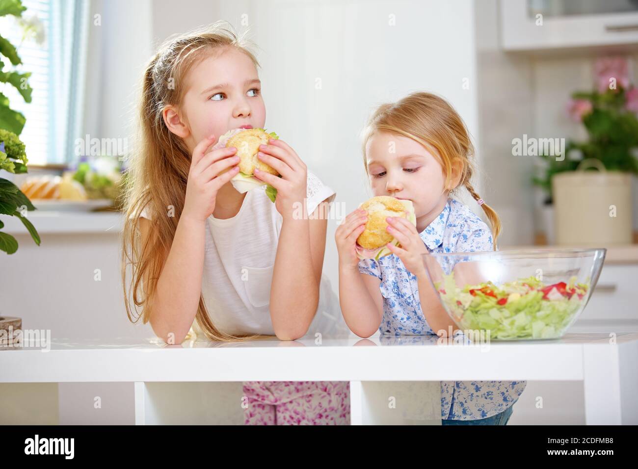 Les filles mangent des sandwiches pour le petit-déjeuner dans la cuisine à côté une salade Banque D'Images