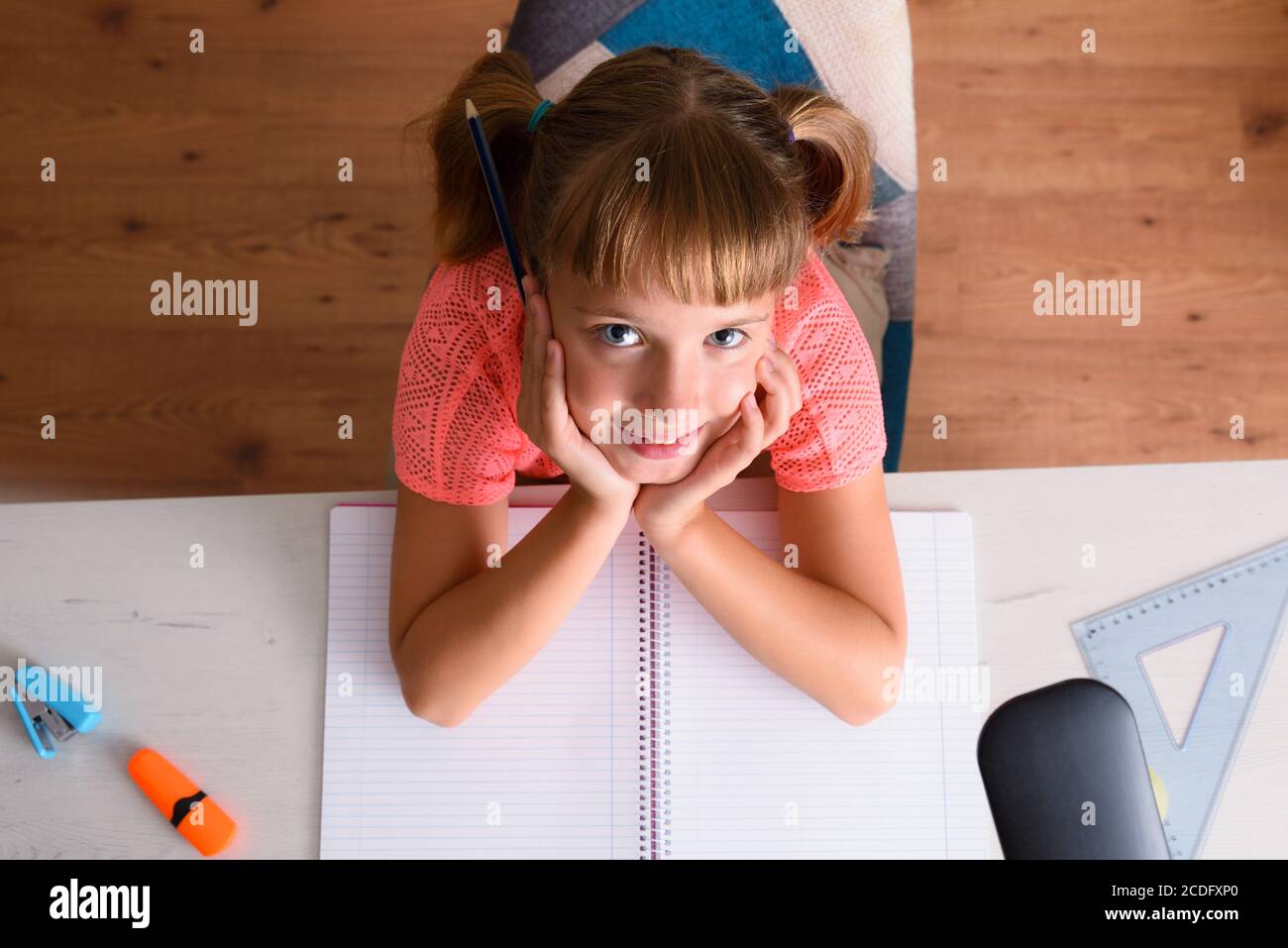 Petite fille souriante étudiant avec ses mains sur le menton sur le bureau. Vue de dessus. Banque D'Images