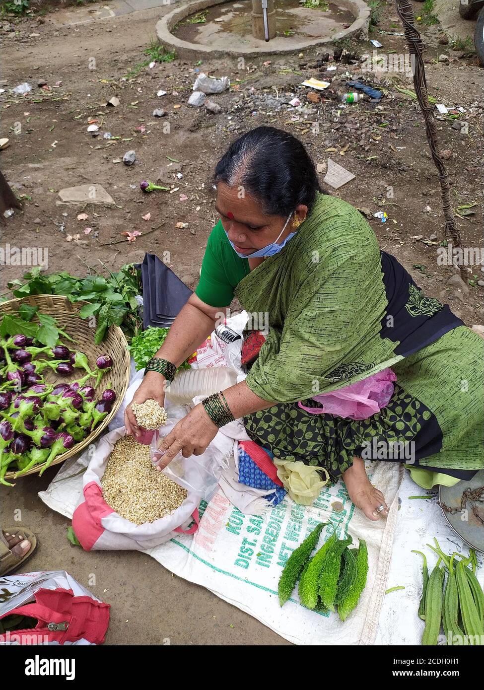 Une dame âgée porte un masque facial et vend des légumes dans la cour du marché. Mesurer les légumineuses à grains de papillon à l'aide d'un ustensile de mesure. Banque D'Images