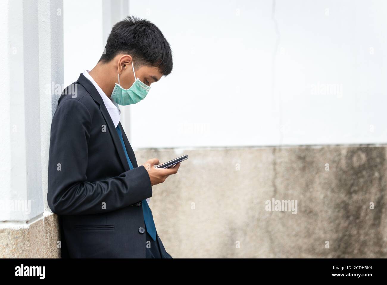Un beau jeune homme d'affaires asiatique utilisant un smartphone. Asiatique jeune homme d'affaires attrayant portant un masque de visage appuyé contre le mur. Banque D'Images