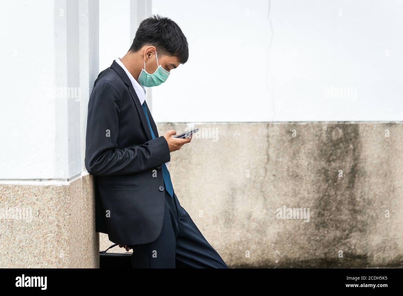 Un beau jeune homme d'affaires asiatique utilisant un smartphone. Asiatique jeune homme d'affaires attrayant portant un masque de visage appuyé contre le mur. Banque D'Images