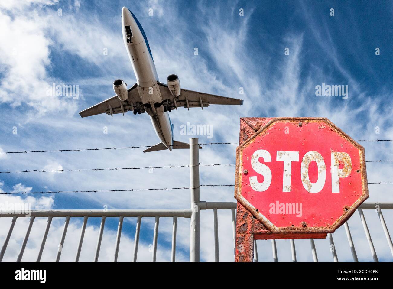 Avion survolant la clôture périphérique de l'aéroport avec le panneau stop en premier plan. Industrie aéronautique, Covid 19, coronavirus, tourisme..., concept. Banque D'Images