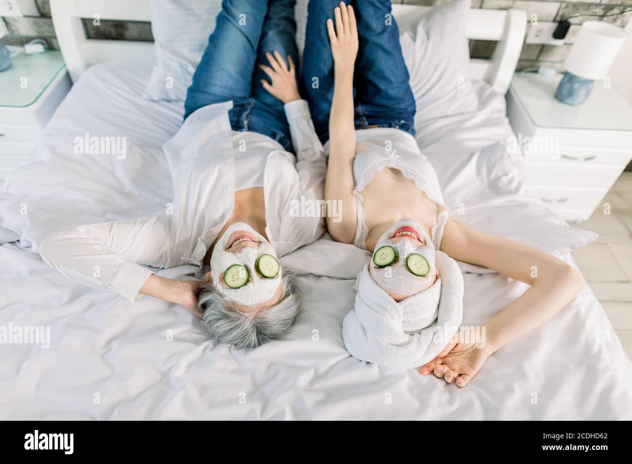 Vue de haut angle de deux femmes charmantes, femme sénior aux cheveux gris et jeune fille avec une serviette sur la tête, allongé sur le lit et profitant de la journée spa avec des masques de visage Banque D'Images