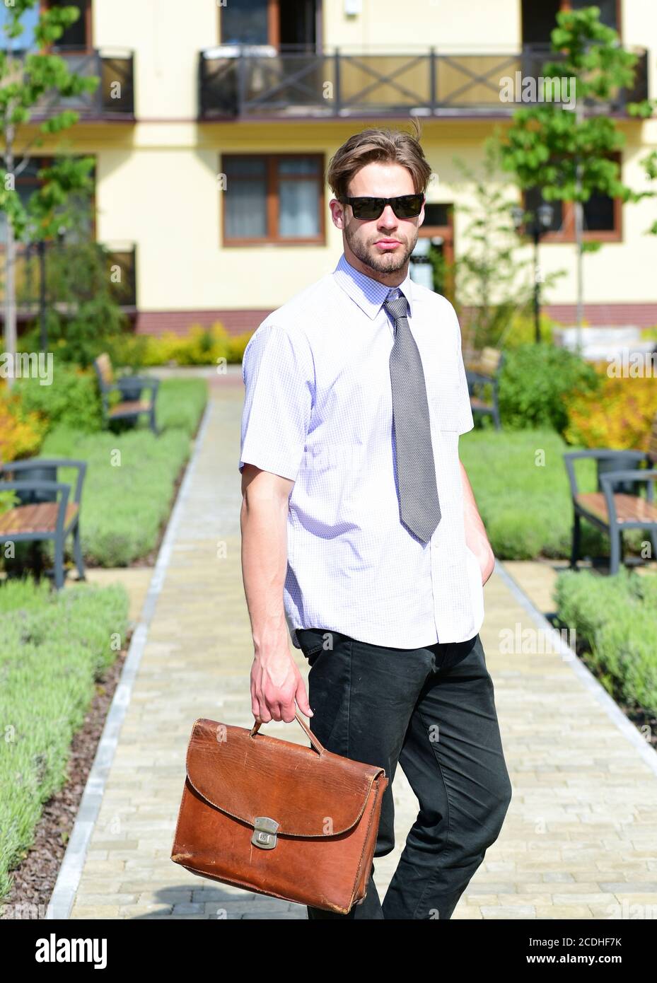 Concept d'affaires et immobilier. L'agent immobilier tient le porte- documents. Jeune homme dans la cour de la maison d'appartement le jour  ensoleillé. Homme en chemise avec cravate ou homme d'affaires avec visage  calme